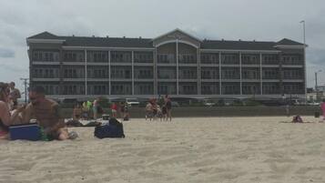 Een hotel met een groot gebouw, meerdere balkons en een zandstrand ervoor.