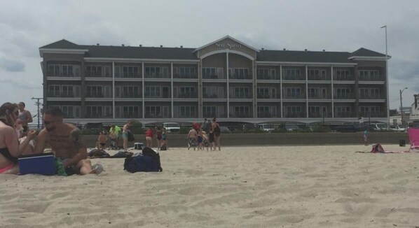 A hotel with a large building, multiple balconies, and a sandy beach area in front.