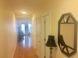 A hallway with wooden flooring, a door, and a wall-mounted lamp.