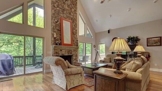 A spacious living room with a stone fireplace, large windows, and a ceiling fan.