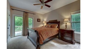 A bedroom with a bed, a nightstand, a ceiling fan, a window with curtains, and a door leading to a balcony.