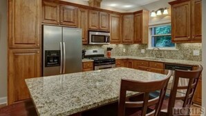 A kitchen with wooden cabinets, granite countertops, stainless steel appliances, and a window with a view.