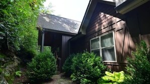 A house with a covered porch, surrounded by dense greenery and a stone pathway.