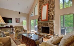 Amplia sala de estar con chimenea de piedra, ventanas grandes y asientos cómodos.