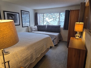 A hotel room with two beds, a window with curtains, a lamp, and framed pictures on the wall.