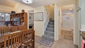 A dining area with a wooden table and chairs, a bookshelf, and a staircase leading to a bathroom.