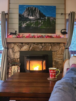 A fireplace with a stone surround, a painting of a mountain landscape above it, and a decorative bird on the mantel. - Camille's Cozy Condo – Inviting Mountain Retreat near Lakes, Trails & Dining (Mammoth Lakes)