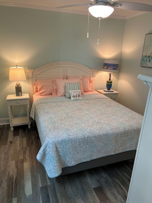 Une chambre à coucher comprenant un lit, des tables de chevet, un ventilateur de plafond et une lampe fixée au mur.