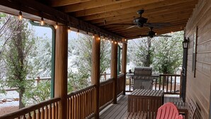 Uma área externa coberta com deck de madeira, churrasqueira e cadeiras Adirondack vermelhas.