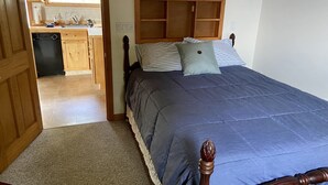 Een slaapkamer met een houten hoofdbord, een bed met een blauwe spreideken, twee kussens en een houten nachtkastje.