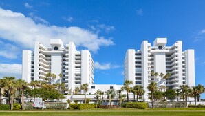Un hôtel moderne composé de deux bâtiments blancs, entouré de palmiers et surplombé d’un ciel d’un bleu limpide.