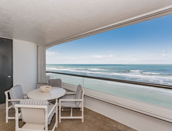 A balcony with a view of the ocean, a round table, and two striped chairs.