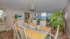 Un coin repas avec une table dressée pour quatre personnes, un lustre et une vue sur l’océan grâce à de grandes fenêtres.