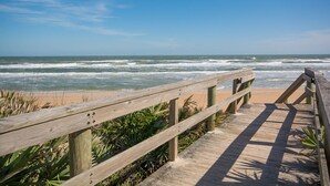 Une promenade en bois mène à une plage où les vagues viennent se briser sur le rivage.