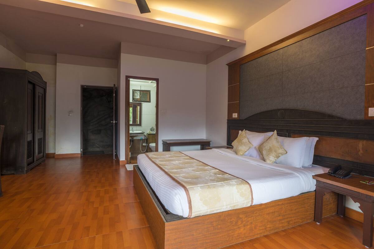 A hotel room with a large bed, wooden headboard, bedside table, and a desk with a chair.