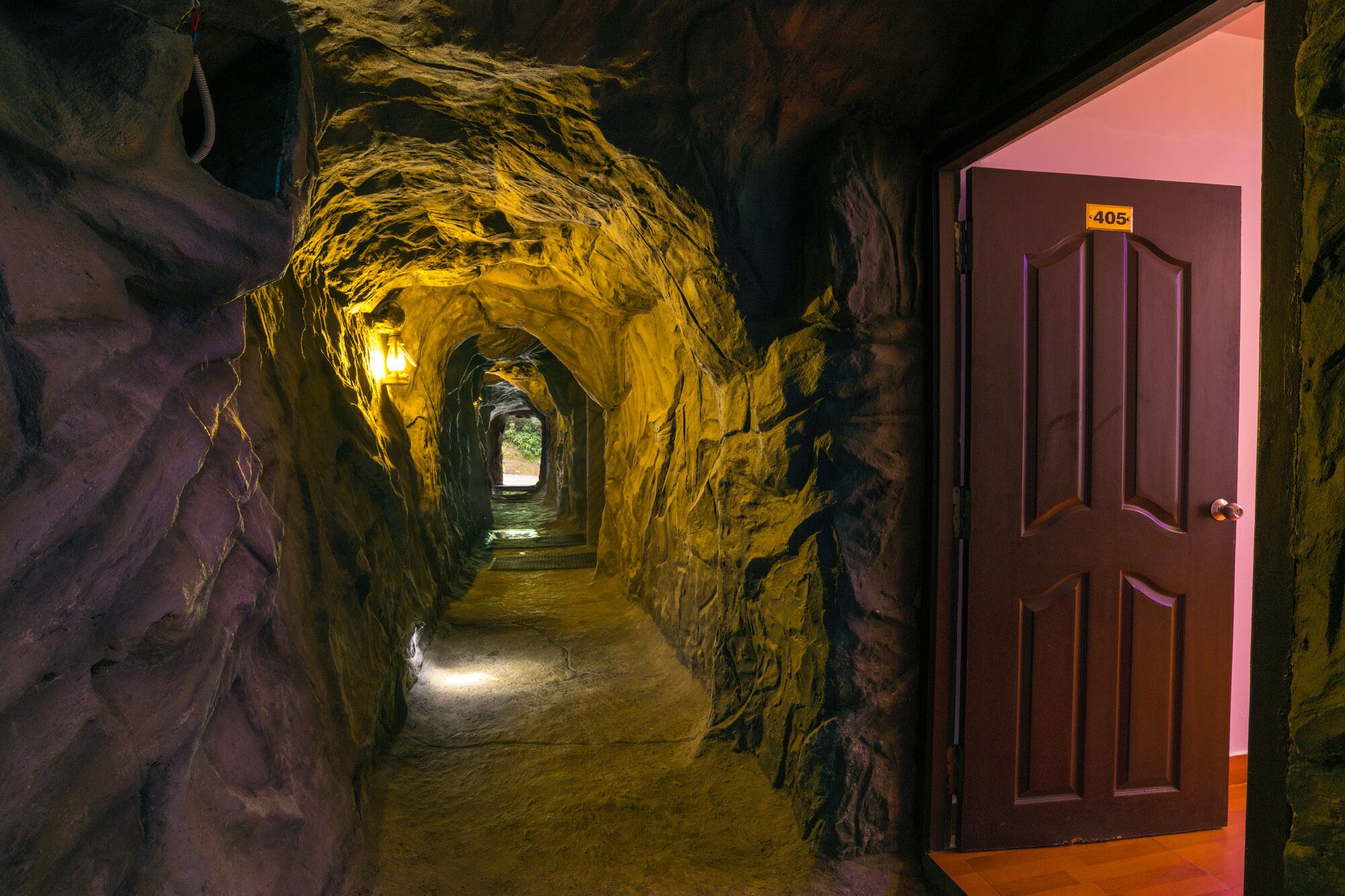 A narrow, dimly lit tunnel with rough, textured walls and a wooden door marked with the number 405.