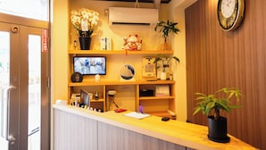 A reception desk with a television, air conditioning unit, and various decorative items including flowers and a clock. - 心乃宿 Kokoro No Yado (Nagoya)