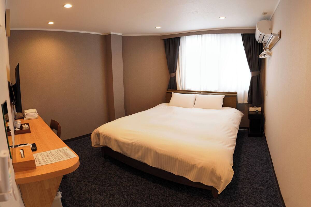 A hotel room with a bed, a desk with a telephone, and a window with curtains.