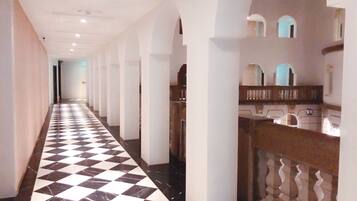 A long hallway with a checkered floor, white walls, and a wooden railing on the right.