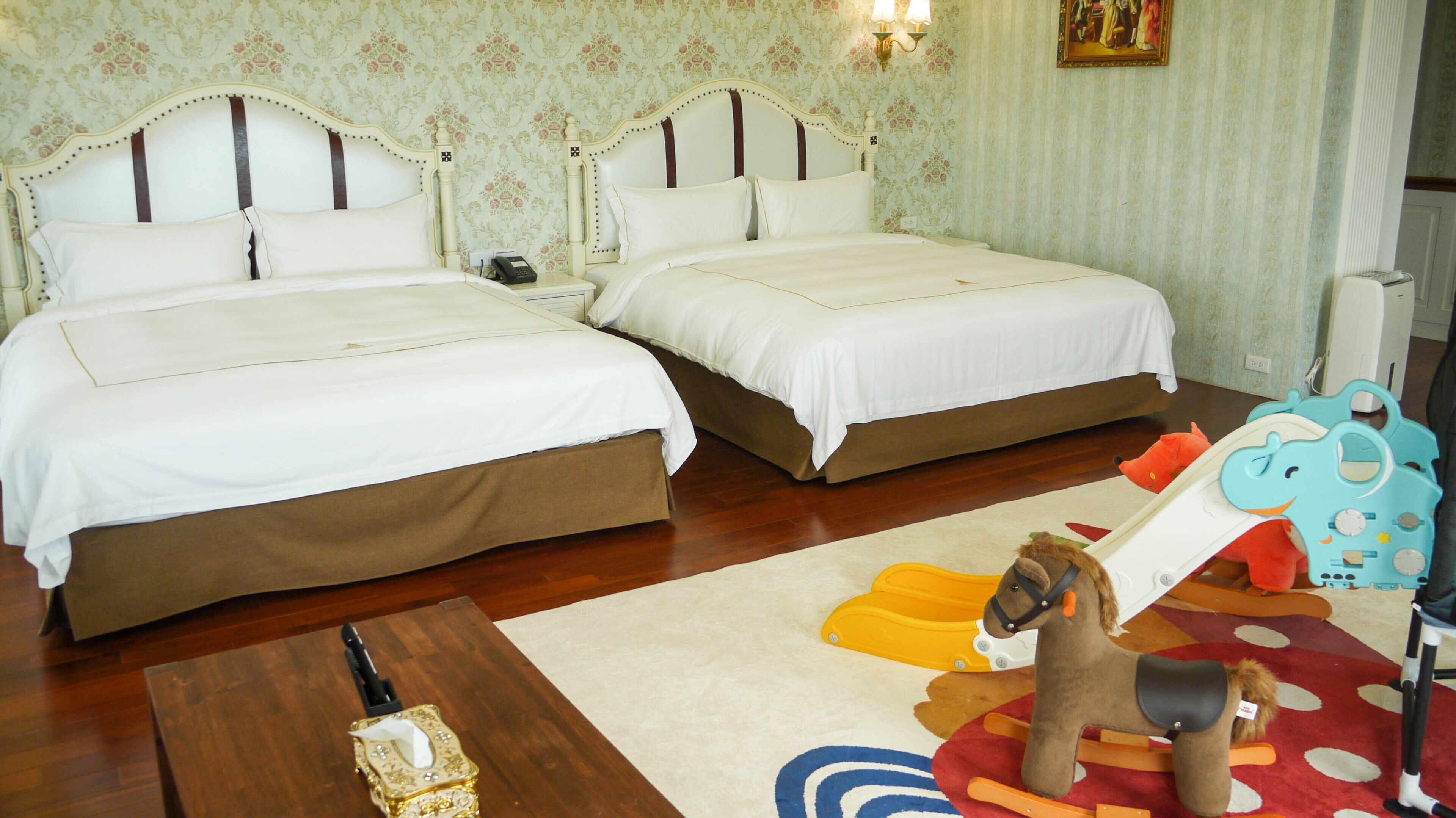 A hotel room with two beds, a wooden coffee table, a toy horse, and a colorful rug.