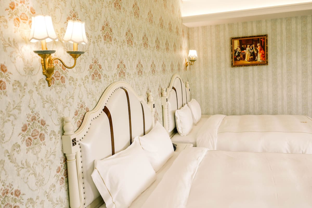 Ein Hotelzimmer im klassischen Design mit einem großen Bett mit weißer Bettwäsche, einem dekorativen Kopfteil und zwei Wandlampen.