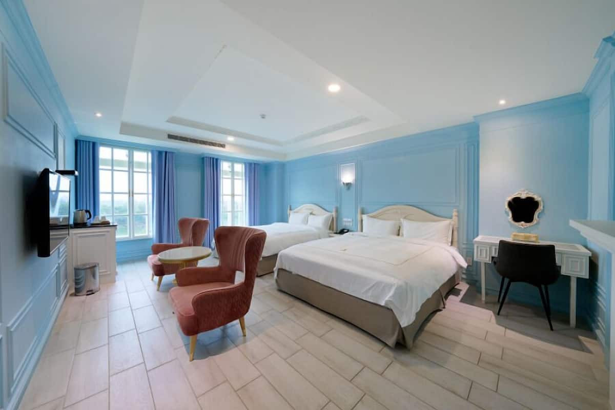 Ein Hotelzimmer mit zwei Betten, einem Schreibtisch, einem Sessel, einem Fernseher und einem Fenster mit Vorhängen.