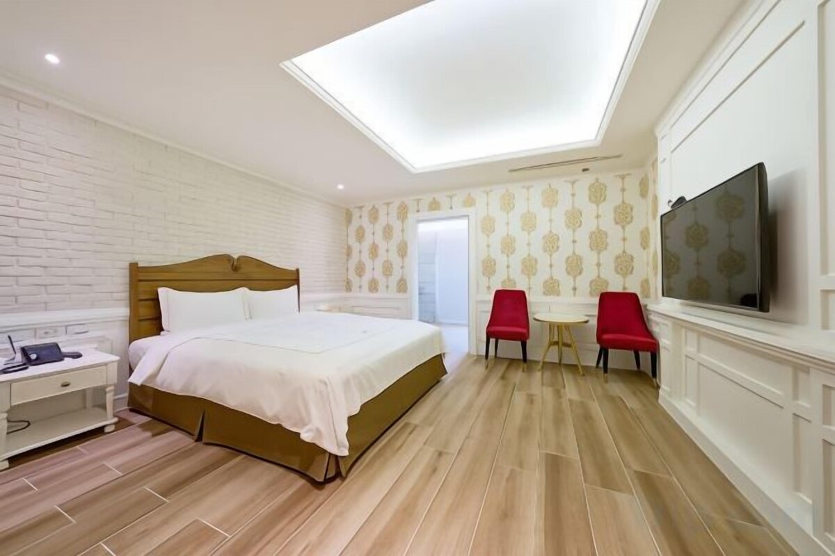 Habitación de hotel con cama, escritorio, televisión y una silla roja.