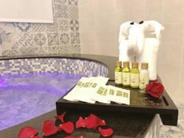 Un baño con bañera, toallas, botellas de aceite de oliva y pétalos de rosa.