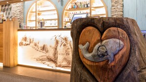 A reception desk with a wooden sculpture of a fish, a chalkboard with prices, and shelves of bottles and glasses in the background. - Landgasthof Hessenmühle (Grossenlueder)