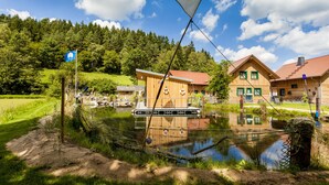 A lakeside wooden cabin with a dock, surrounded by lush greenery and a clear sky. - Landgasthof Hessenmühle (Grossenlueder)
