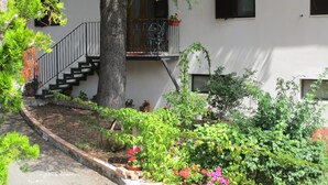 A residential building with a staircase leading to a balcony, surrounded by lush greenery and potted plants. - Podere La Piana (Fivizzano)