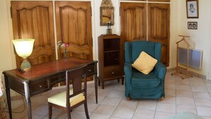 Una habitación con paneles de madera, un escritorio con lámpara, un sillón azul aguamarina con cojín y un perchero.