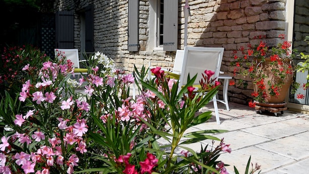 Un edificio de piedra con un patio, mobiliario exterior y plantas con flores.