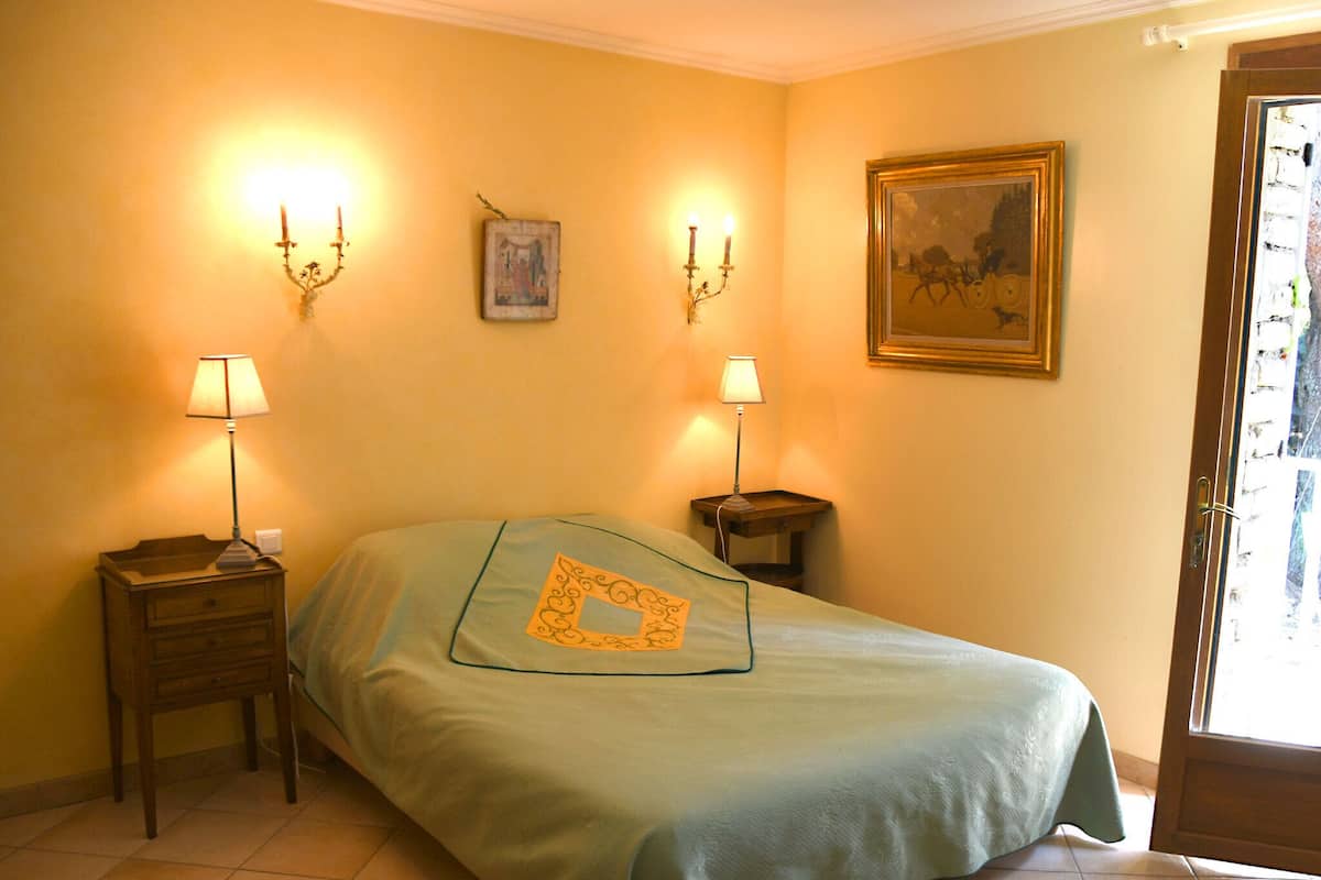 Ein Zimmer mit einem Bett, zwei Nachttischen mit Lampen, einem Wandbild und einer Tür mit Blick.
