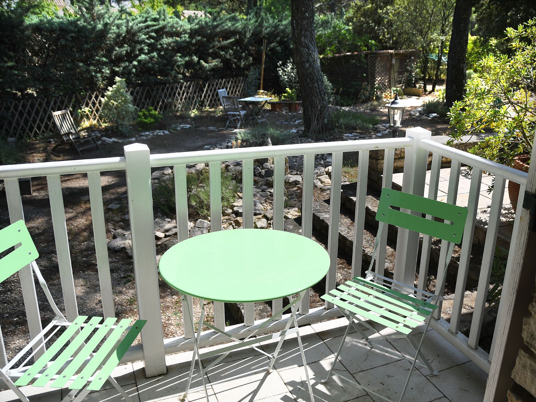 A patio with a white railing, a round table, and two green chairs.