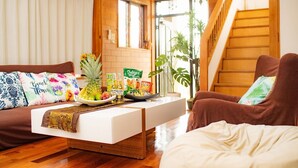 A hotel lobby with a wooden staircase, a reception desk, and a sofa with colorful pillows. - MK Garden (Okinawa)