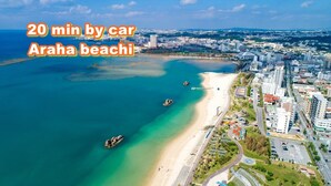 An aerial view of Arah beach with clear turquoise waters, a sandy beach, and a cityscape in the background. - MK Garden (Okinawa)