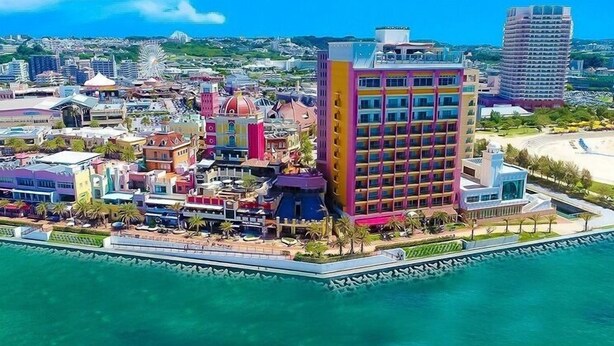 An aerial view of a coastal hotel with a central building, multiple colorful structures, and a beach area. - MK Garden (Okinawa)