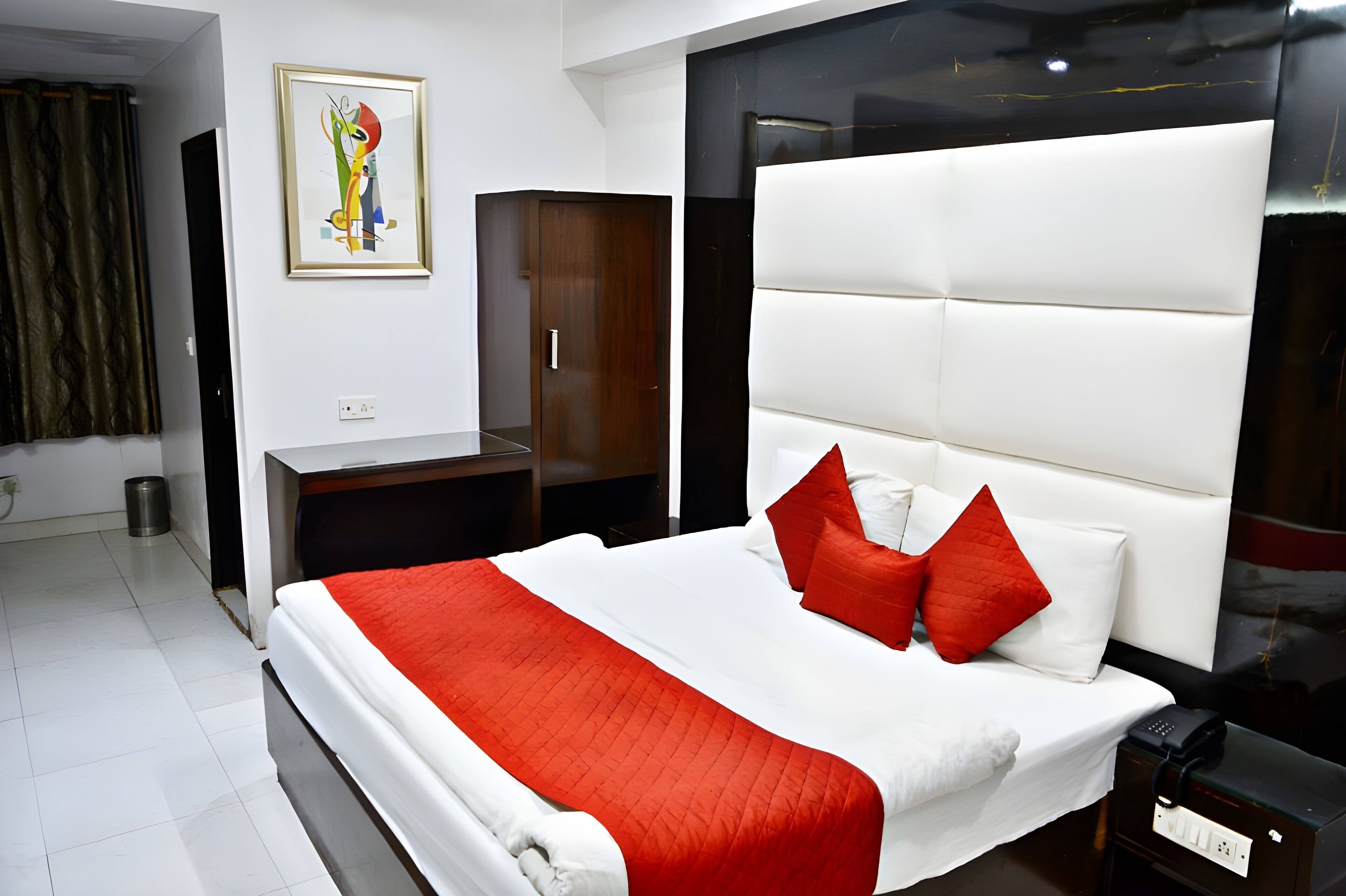 A modern hotel room with a large bed, a wardrobe, a painting on the wall, and a black-framed mirror.