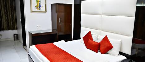 A modern hotel room with a large bed, a wardrobe, a painting on the wall, and a black-framed mirror.