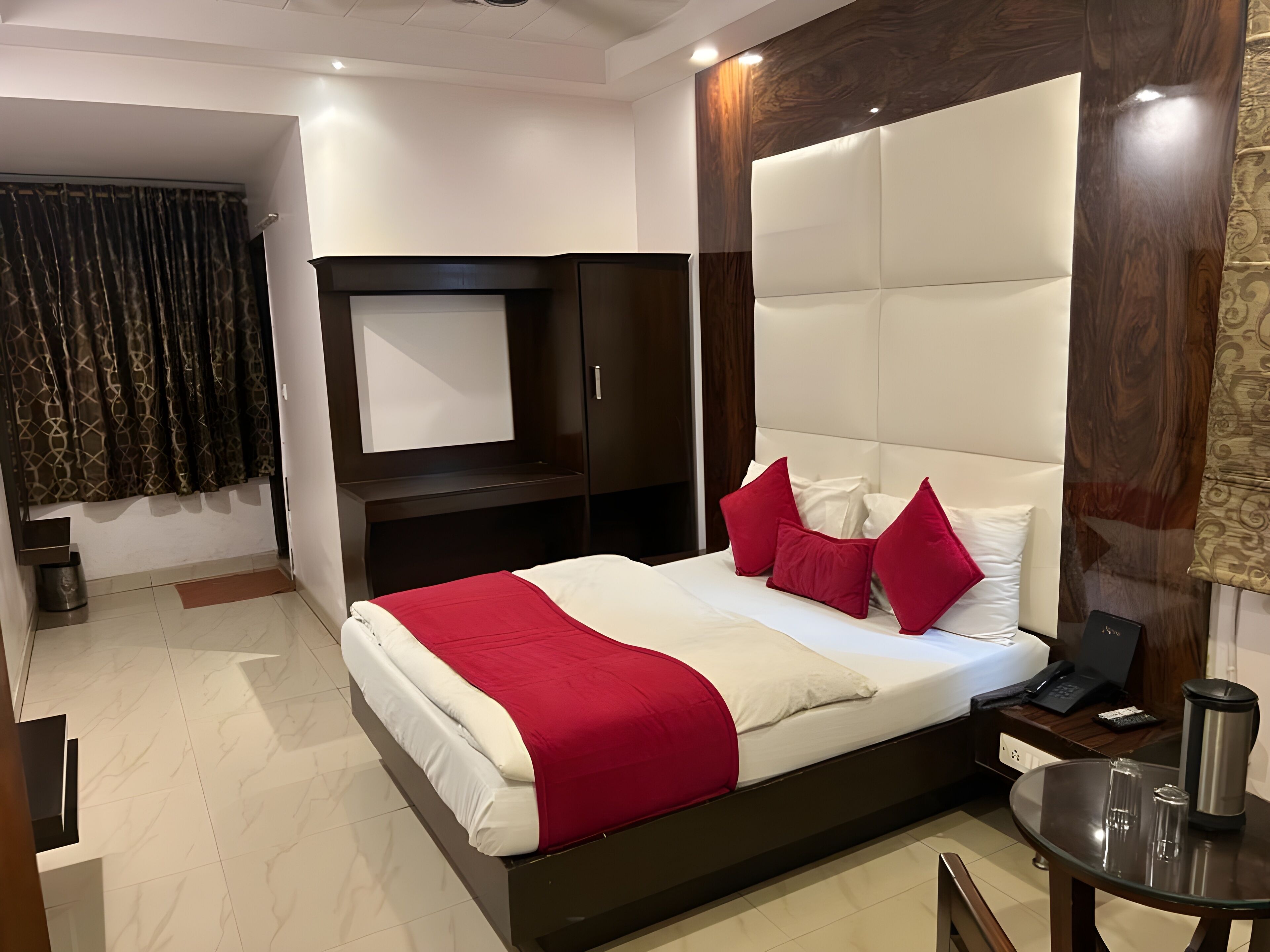 A hotel room with a large bed, a TV mounted on the wall, a desk with a chair, and a small table with a coffee maker.