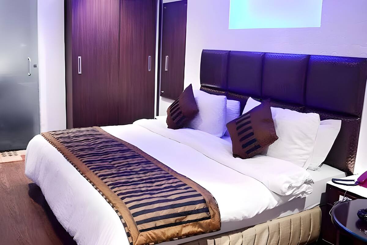 A modern hotel room with a large bed, a headboard, and a bedside table.