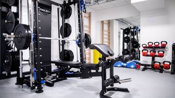 Un gimnasio con equipo de levantamiento de pesas, incluyendo una jaula de sentadillas y mancuernas.