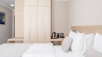 A hotel room with a bed, a wooden wardrobe, a bedside table with a coffee maker, and a painting on the wall.