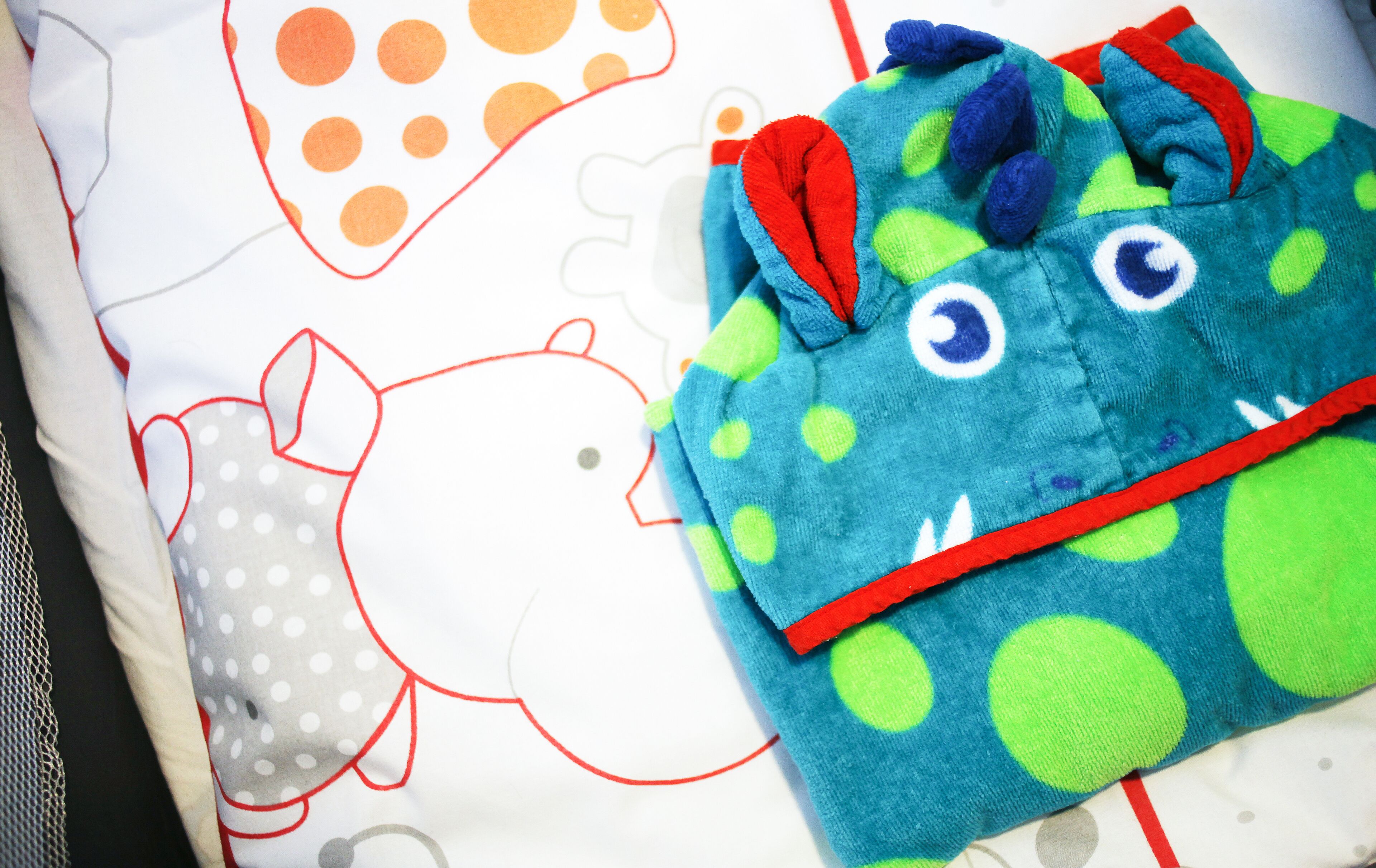 A bed with a white sheet featuring cartoon characters and a blue blanket with a cartoon monster design.