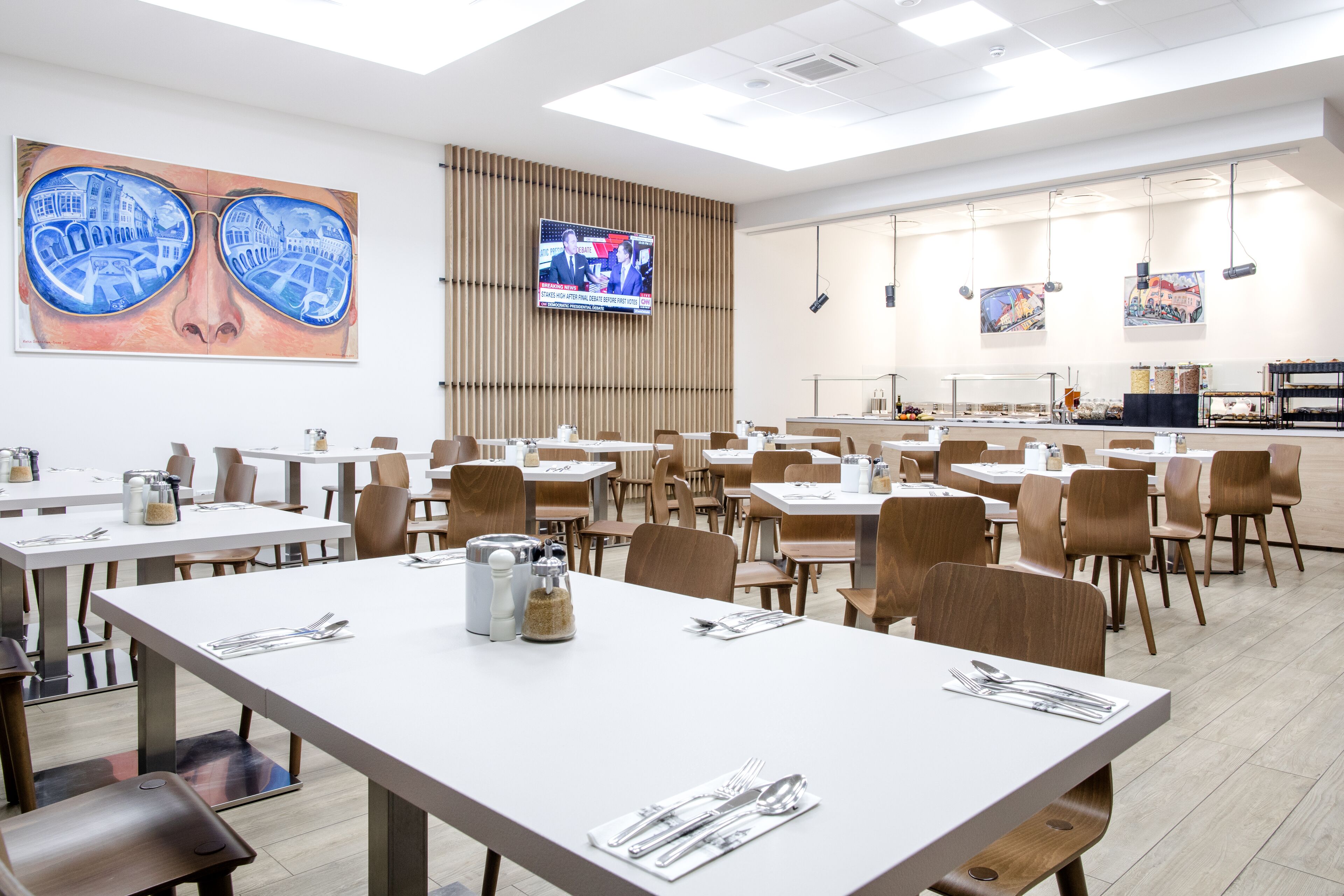 Un grand espace dédié à la salle à manger, avec plusieurs tables et chaises, un écran de télévision et des œuvres d’art accrochées aux murs.