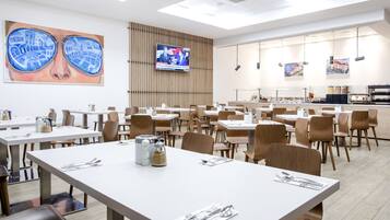 Un grand espace dédié à la salle à manger, avec plusieurs tables et chaises, un écran de télévision et des œuvres d’art accrochées aux murs.