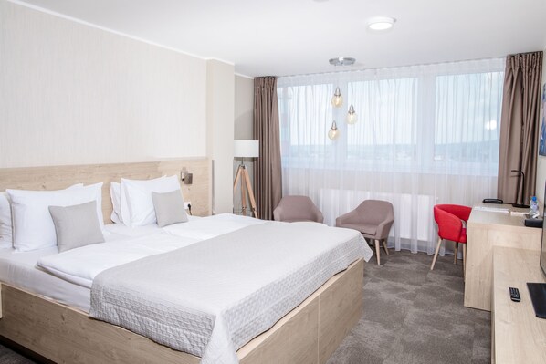 Une chambre d’hôtel avec un grand lit, un bureau, une chaise et une fenêtre avec des rideaux.