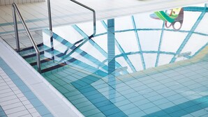 Una piscina con agua cristalina, suelo de azulejos y barandillas de metal.