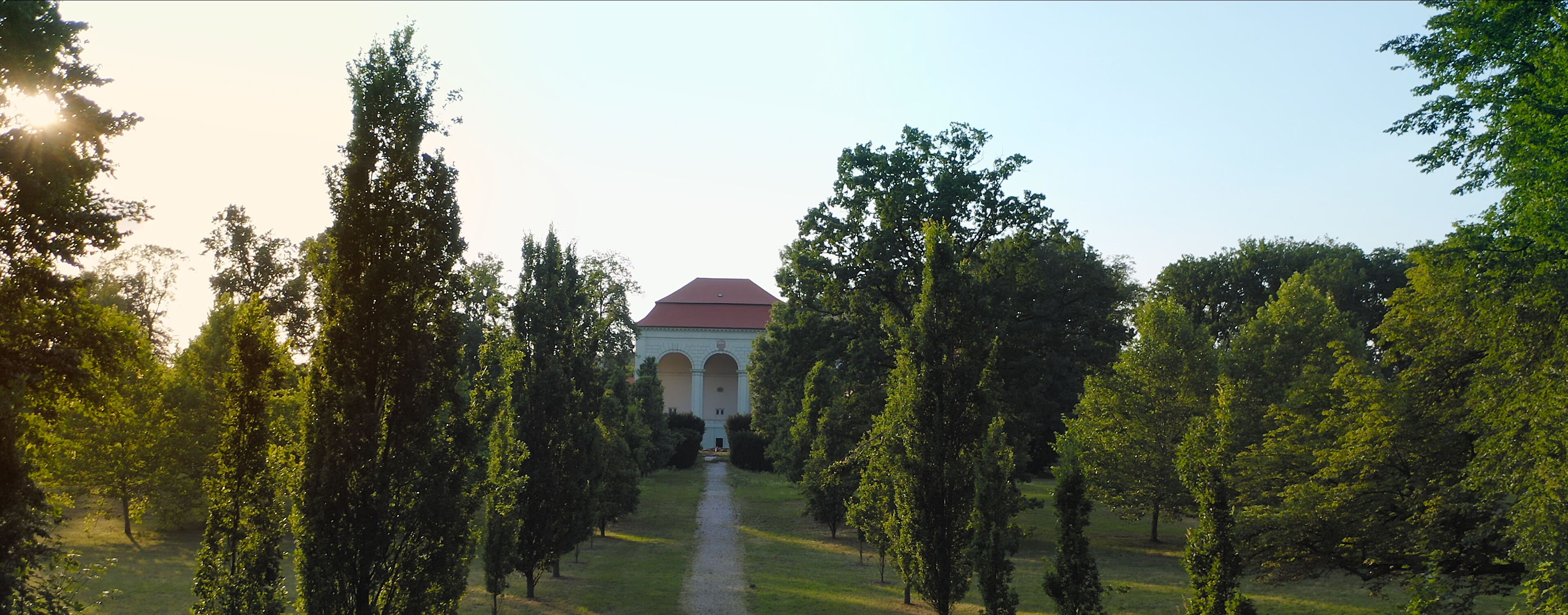 A pathway leading to a building with a red roof, surrounded by trees.